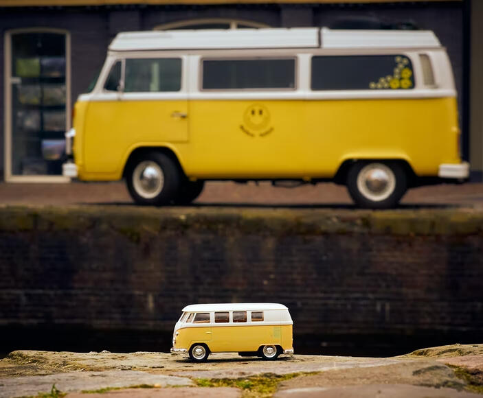 Dos furgonetas Volkswagen amarillas, una delante pequeña, es un juguete, otra al fondo grande tamaño real.